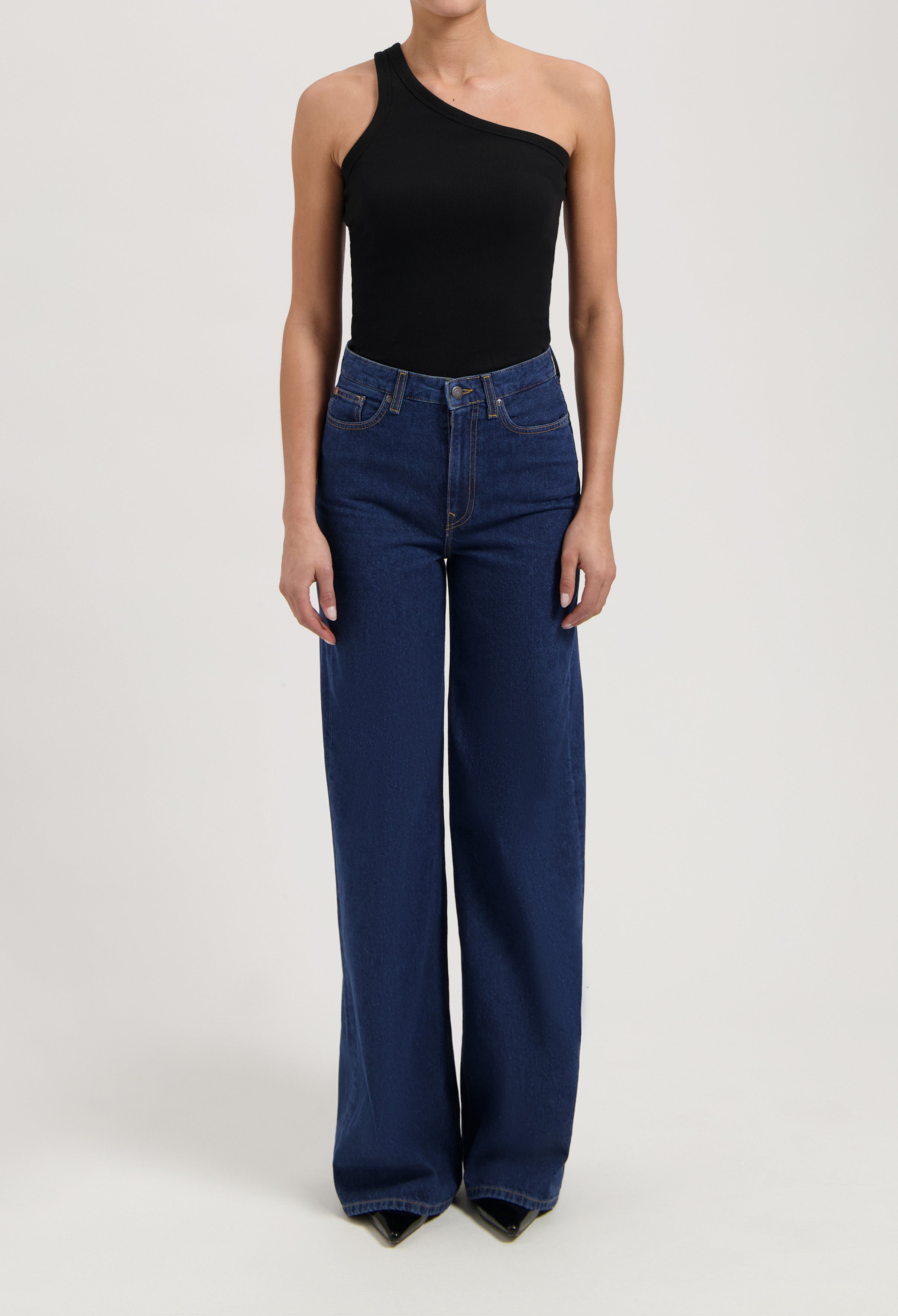 Wide-leg high-waisted jeans in deep blue, paired with a black one-shoulder top, showing a casual yet stylish look.