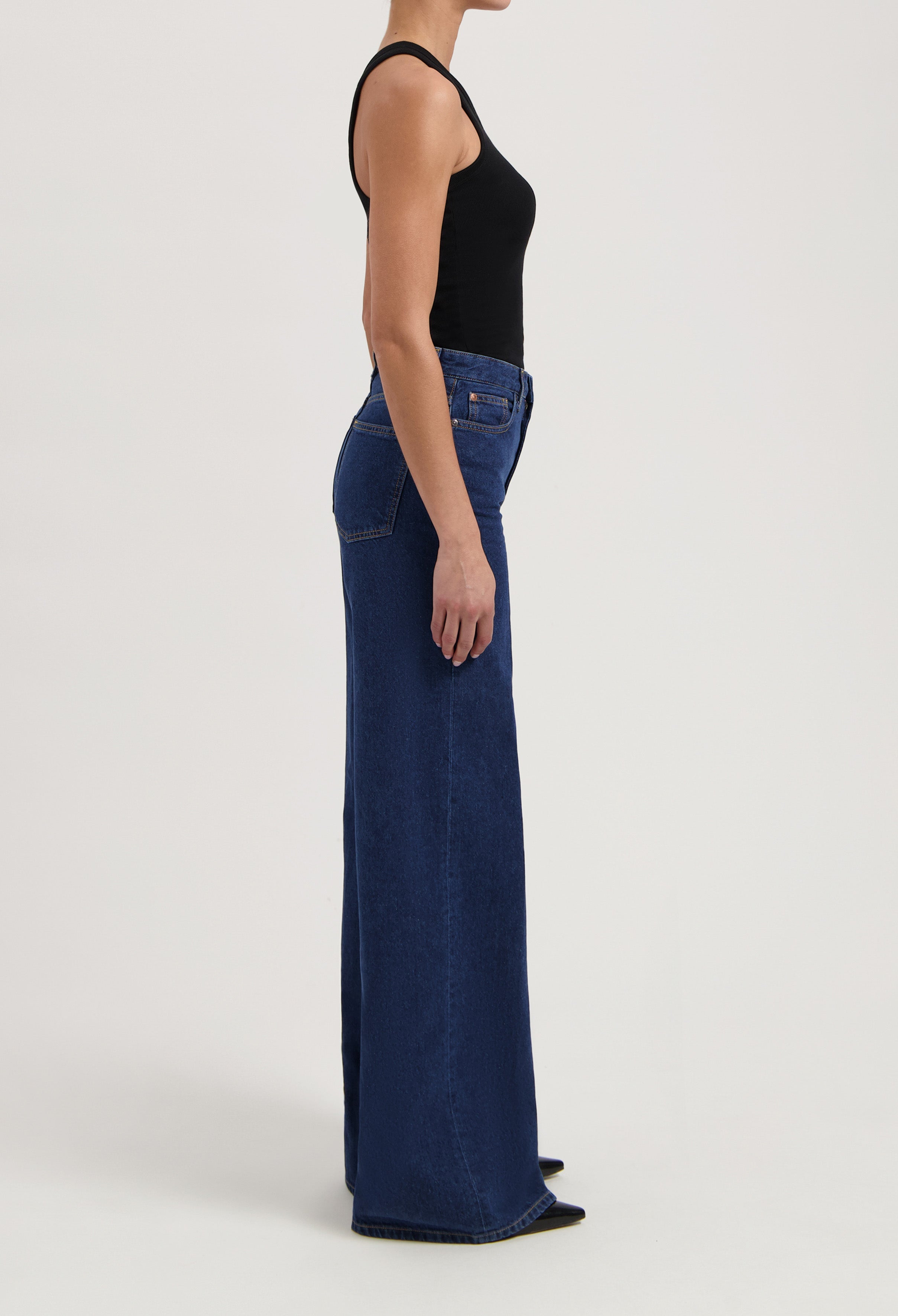 Wide-leg blue jeans made from denim, shown in profile view with a fitted black tank top, highlighting the high-rise design.