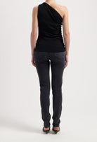 One-shoulder black top paired with dark gray slim-fit jeans and black heels, showing a sleek, minimalist style.