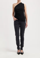 Model wearing an asymmetrical black sleeveless top paired with dark gray slim-fit jeans and black pointed flats.