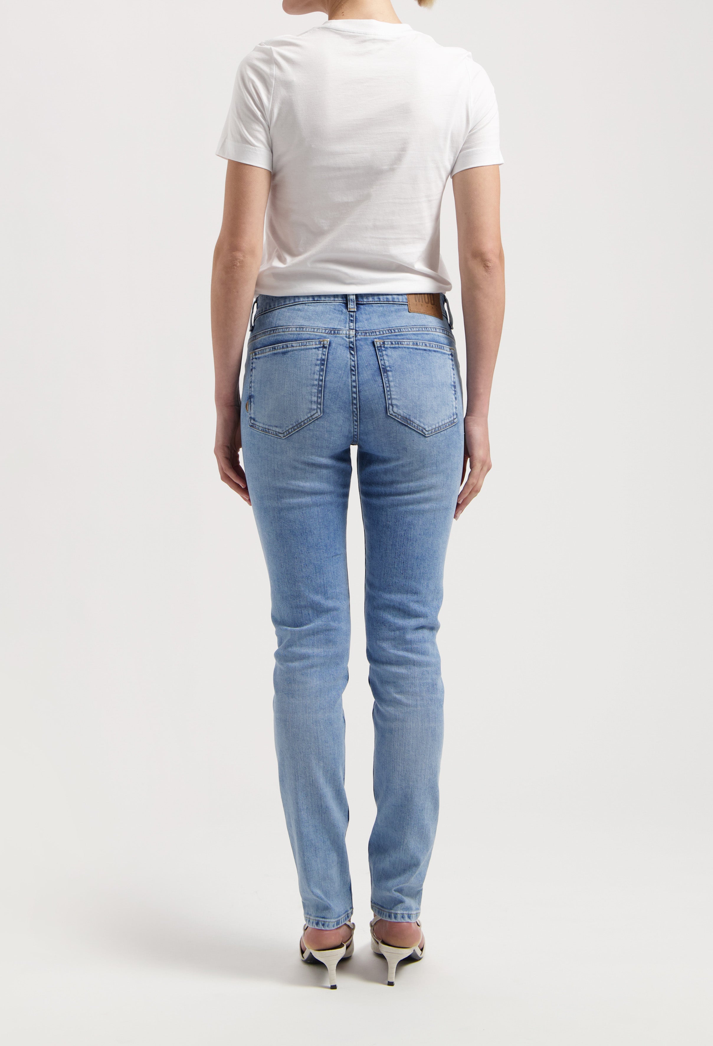 Back view of light blue denim jeans paired with a simple white T-shirt, worn by a model standing in heels.
