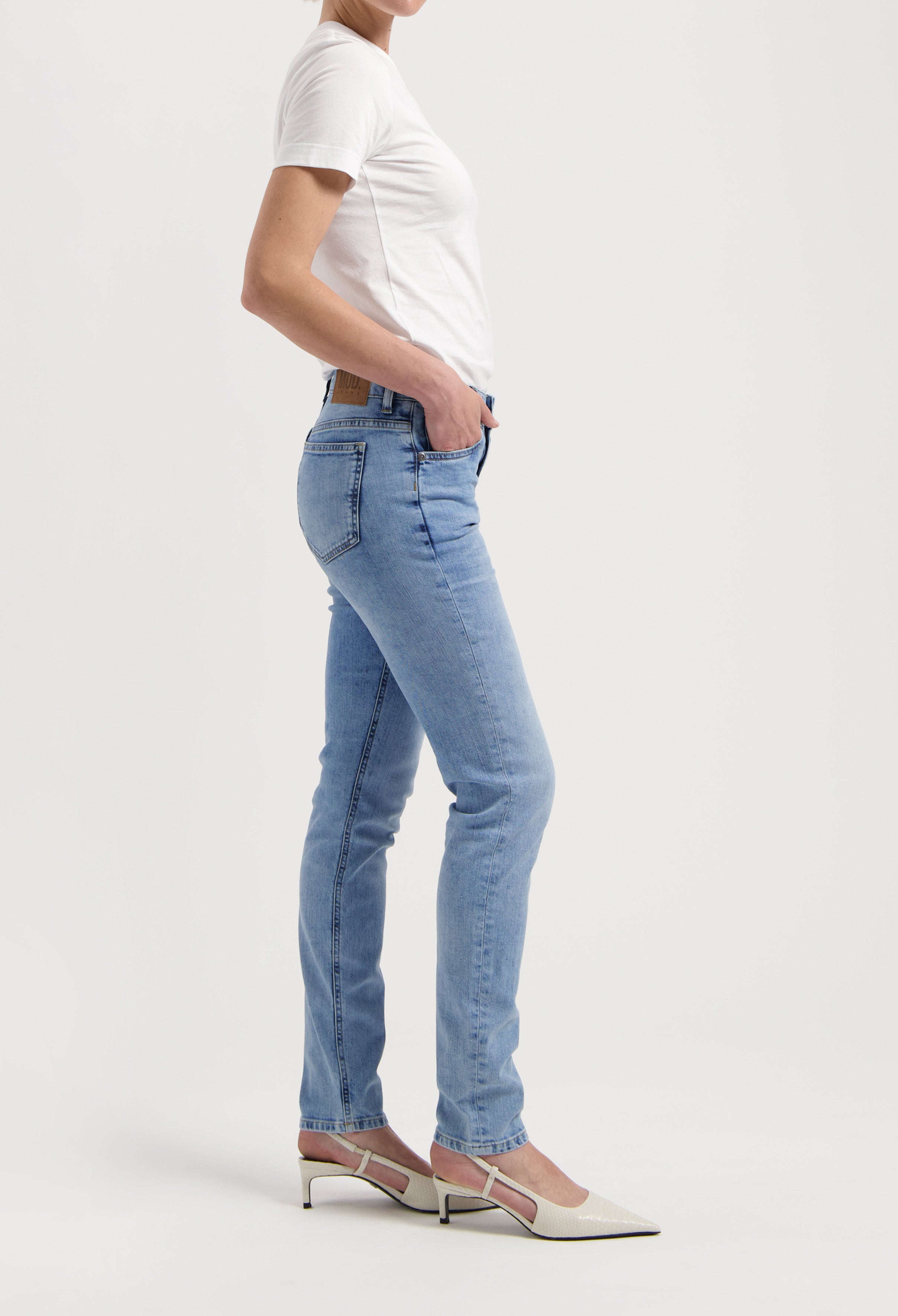 Light blue denim slim-fit jeans with a high-waist design, worn with a white short-sleeve top and white pointed heels.