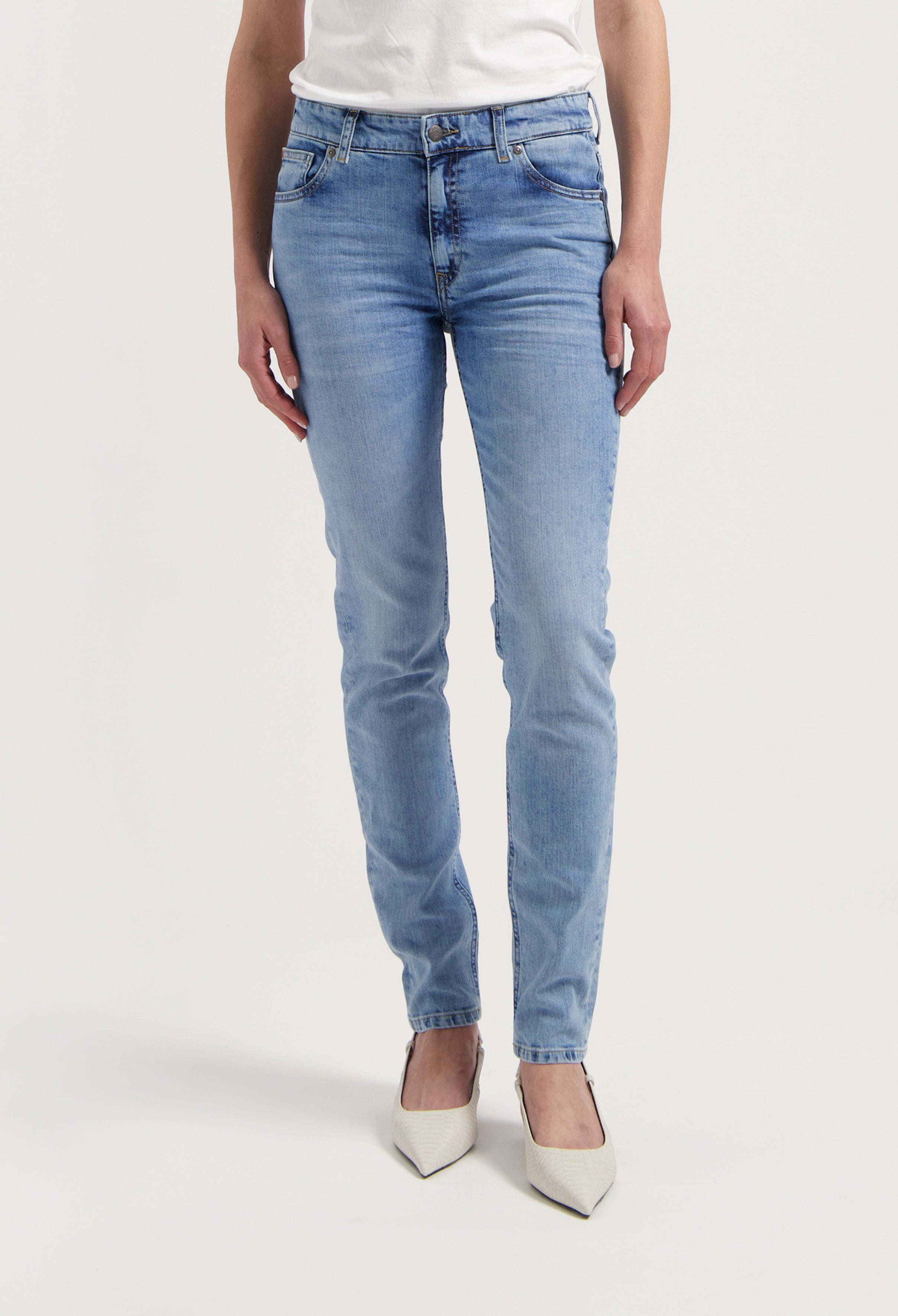 Light blue slim-fit jeans made from denim, paired with a white top and pointed white heels, showcased on a person standing.