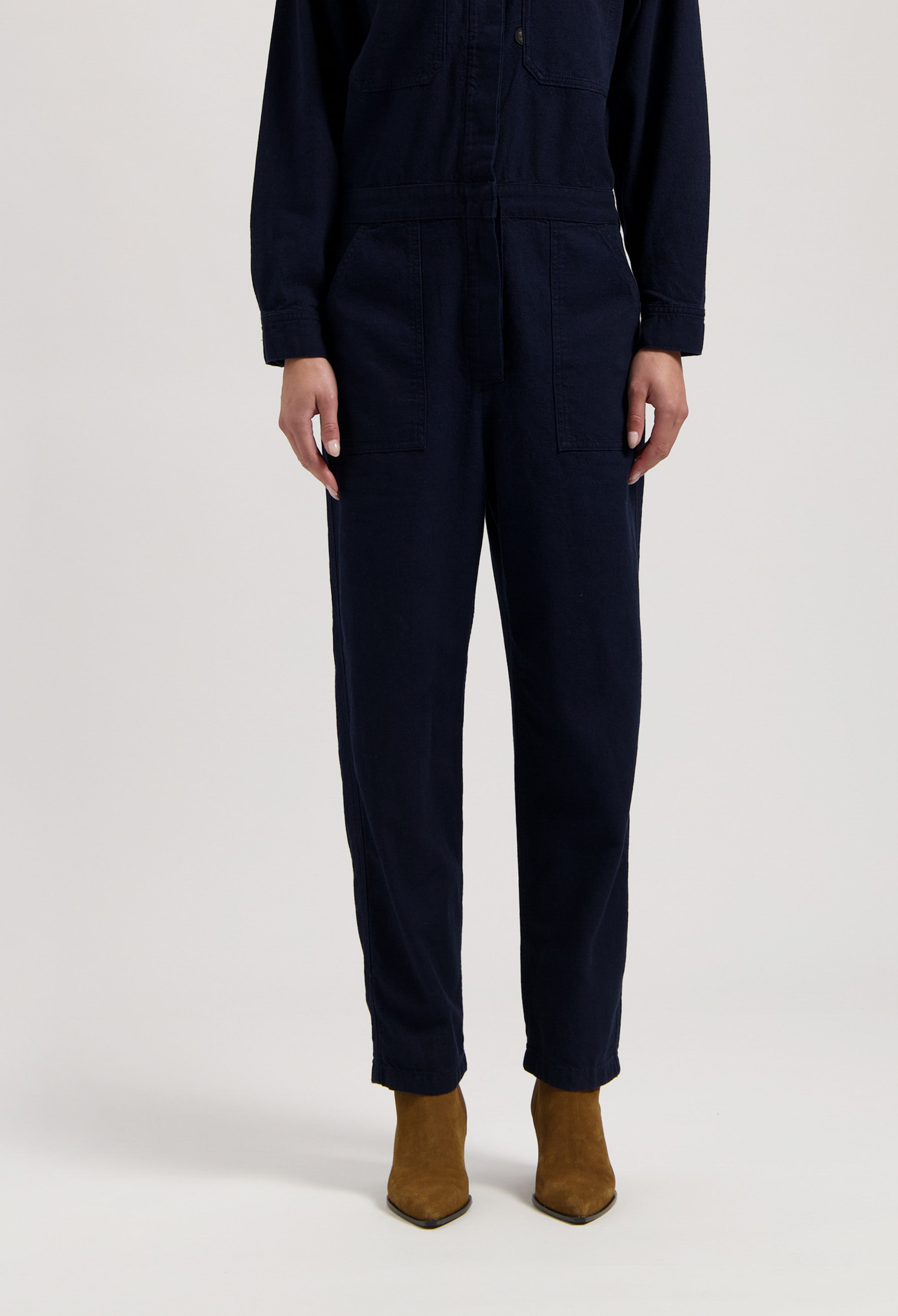 Dark navy long-sleeve jumpsuit with front pockets, paired with brown suede ankle boots.