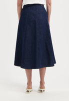 Dark blue denim A-line skirt with seam detailing, worn with a white top, highlighting the skirt's high-waisted fit and flow.