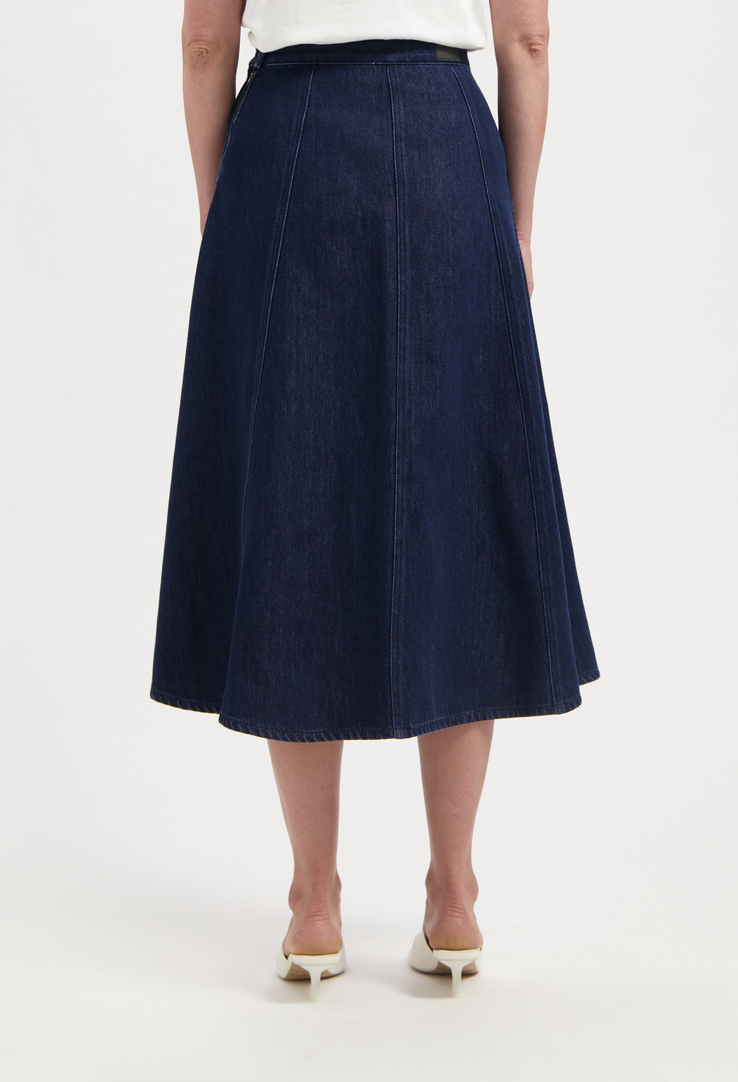 Dark blue denim A-line skirt with seam detailing, worn with a white top, highlighting the skirt's high-waisted fit and flow.