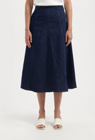 Dark blue, A-line denim skirt worn with a white top, showcasing a classic midi length and vertical seam detailing.