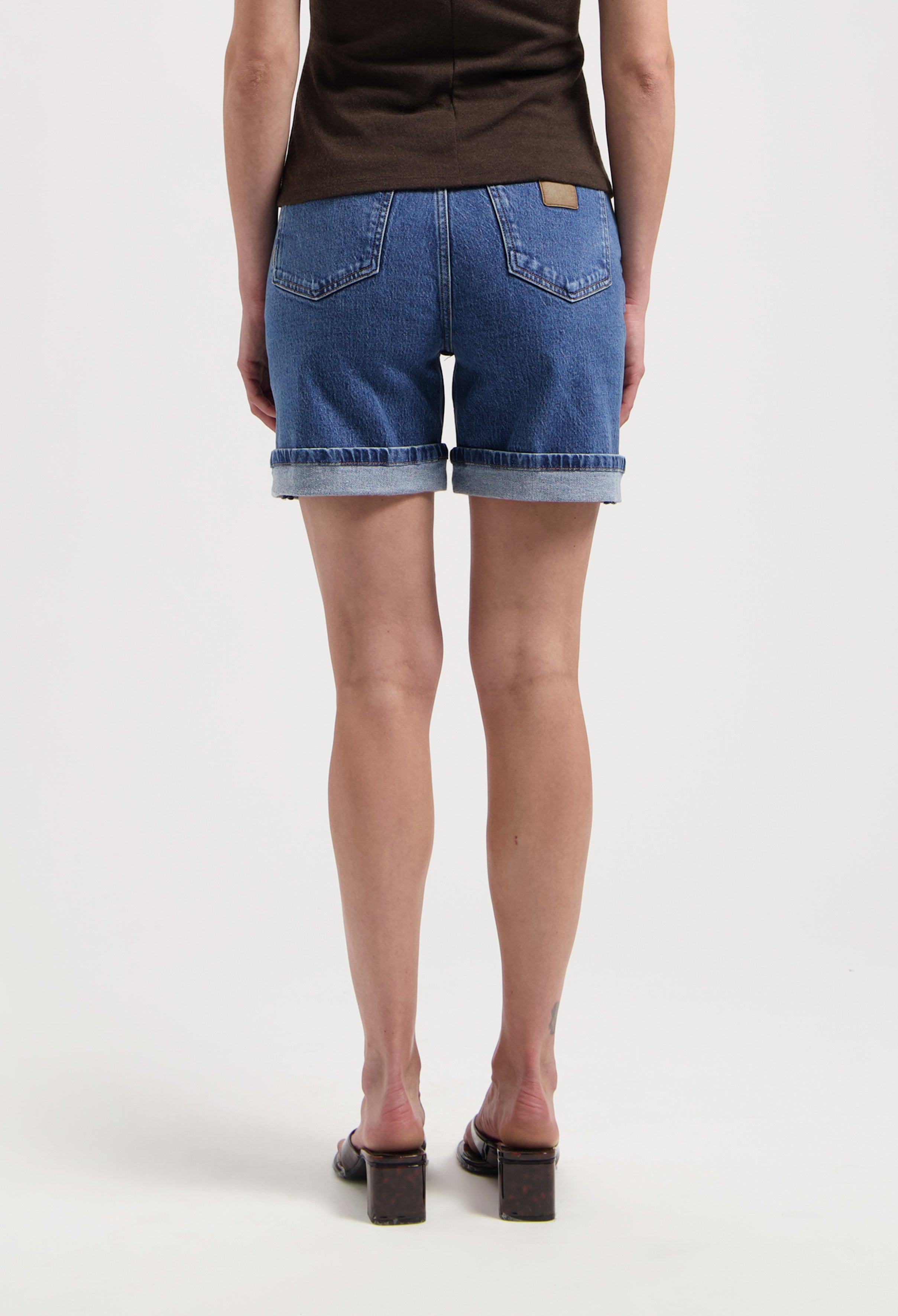 High-waisted denim shorts in classic blue, featuring cuffed hems and paired with a dark brown top, highlighting casual style.