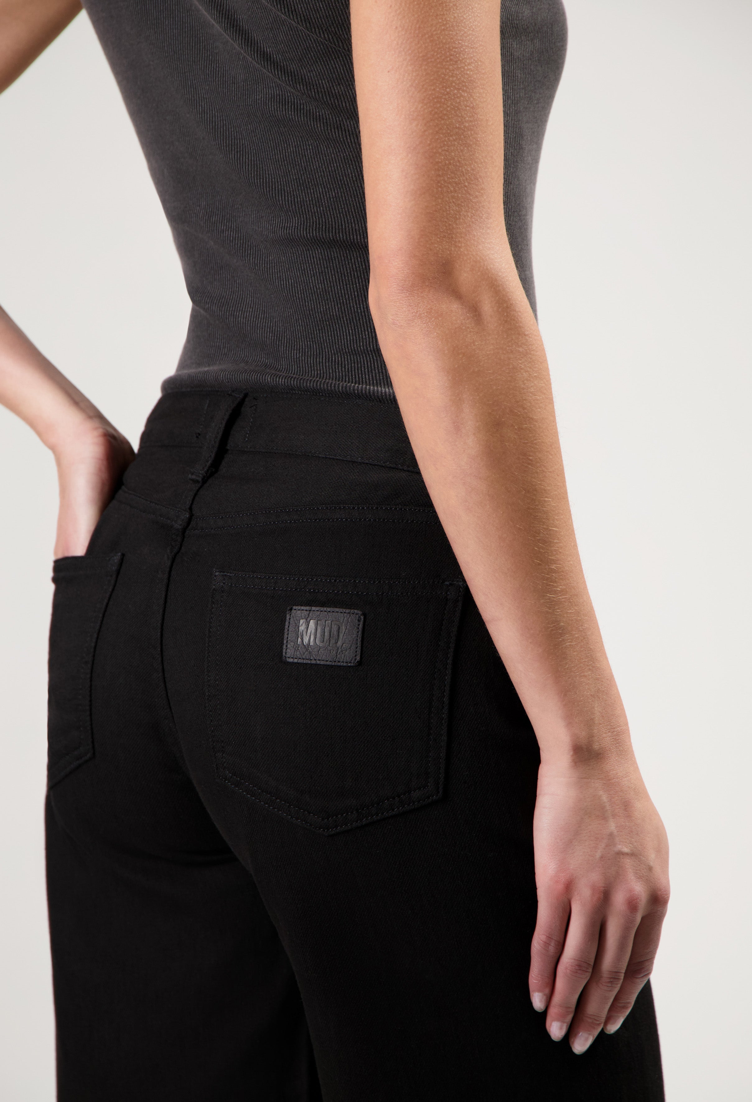 Black MUD jeans made from organic cotton, featuring a high-waisted slim-fit design, paired with a sleeveless dark gray top.