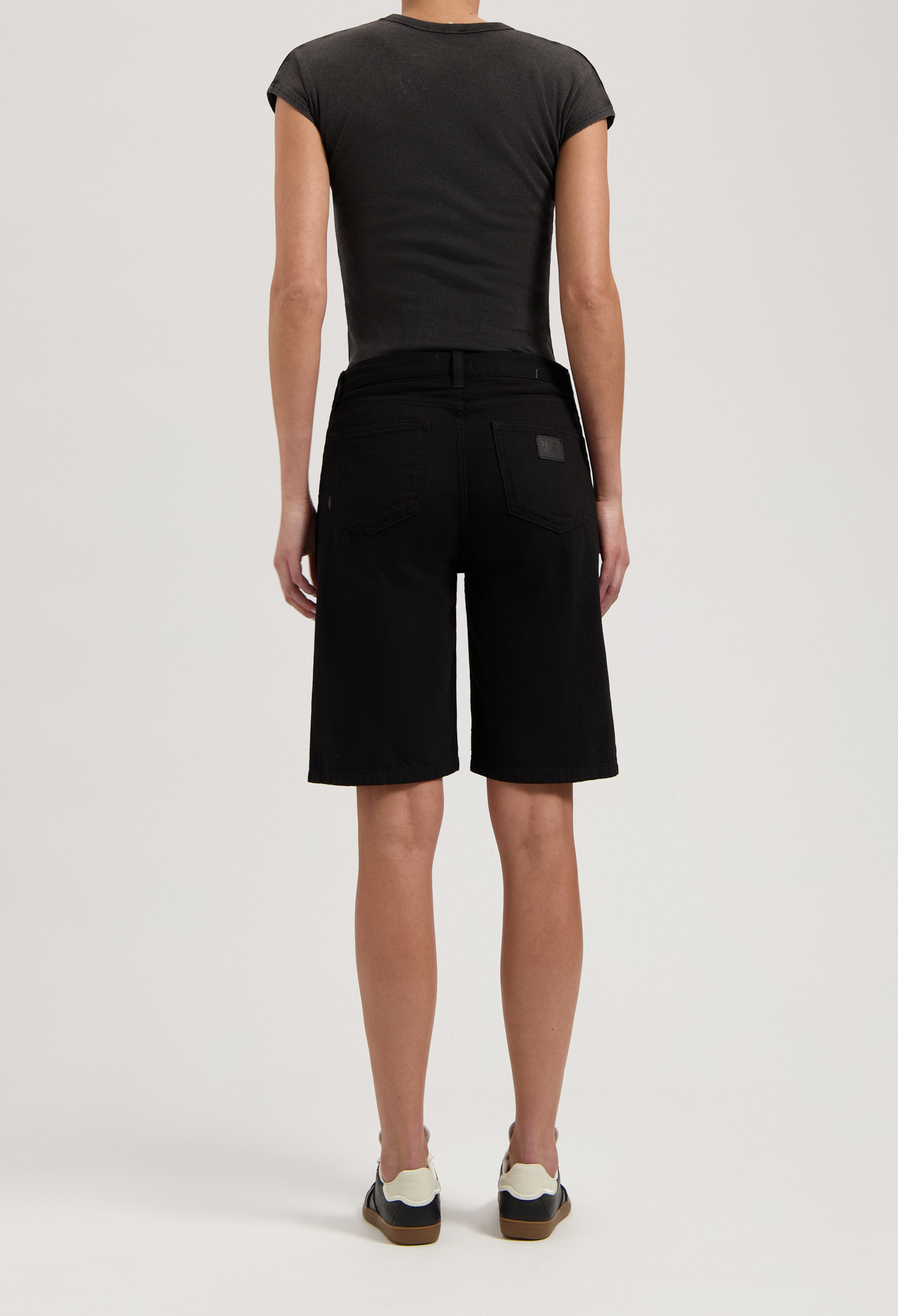 Black denim shorts styled with a fitted dark gray top and casual sneakers, highlighting a modern summer outfit.