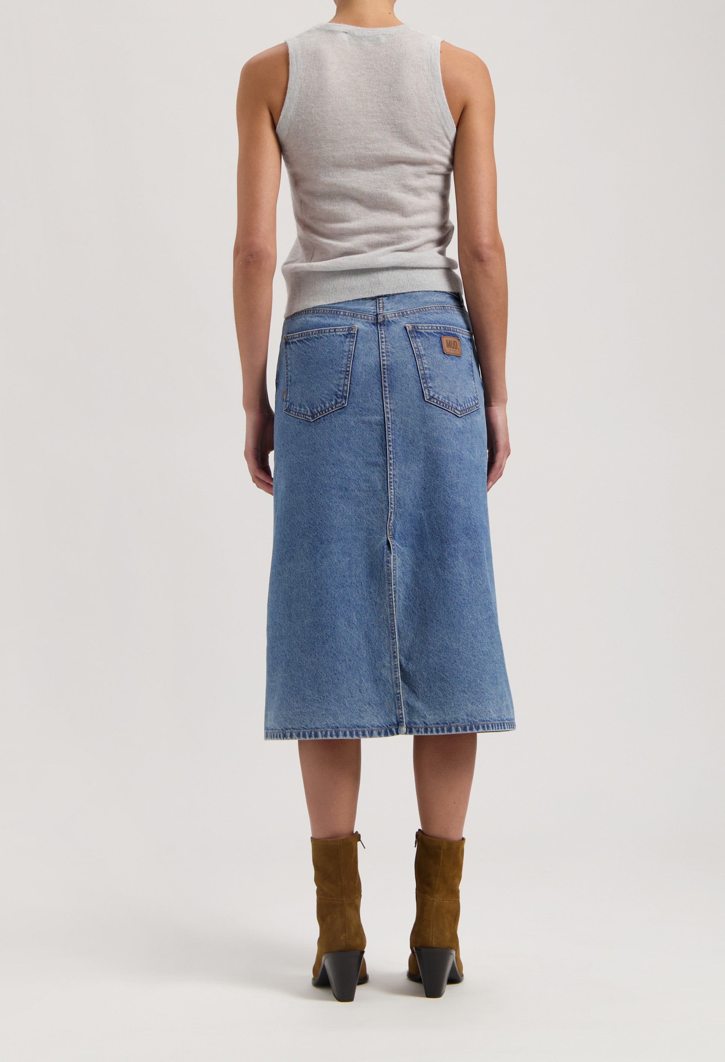 Back view of a light gray sleeveless top paired with a knee-length denim MUD Jeans skirt and brown suede ankle boots.