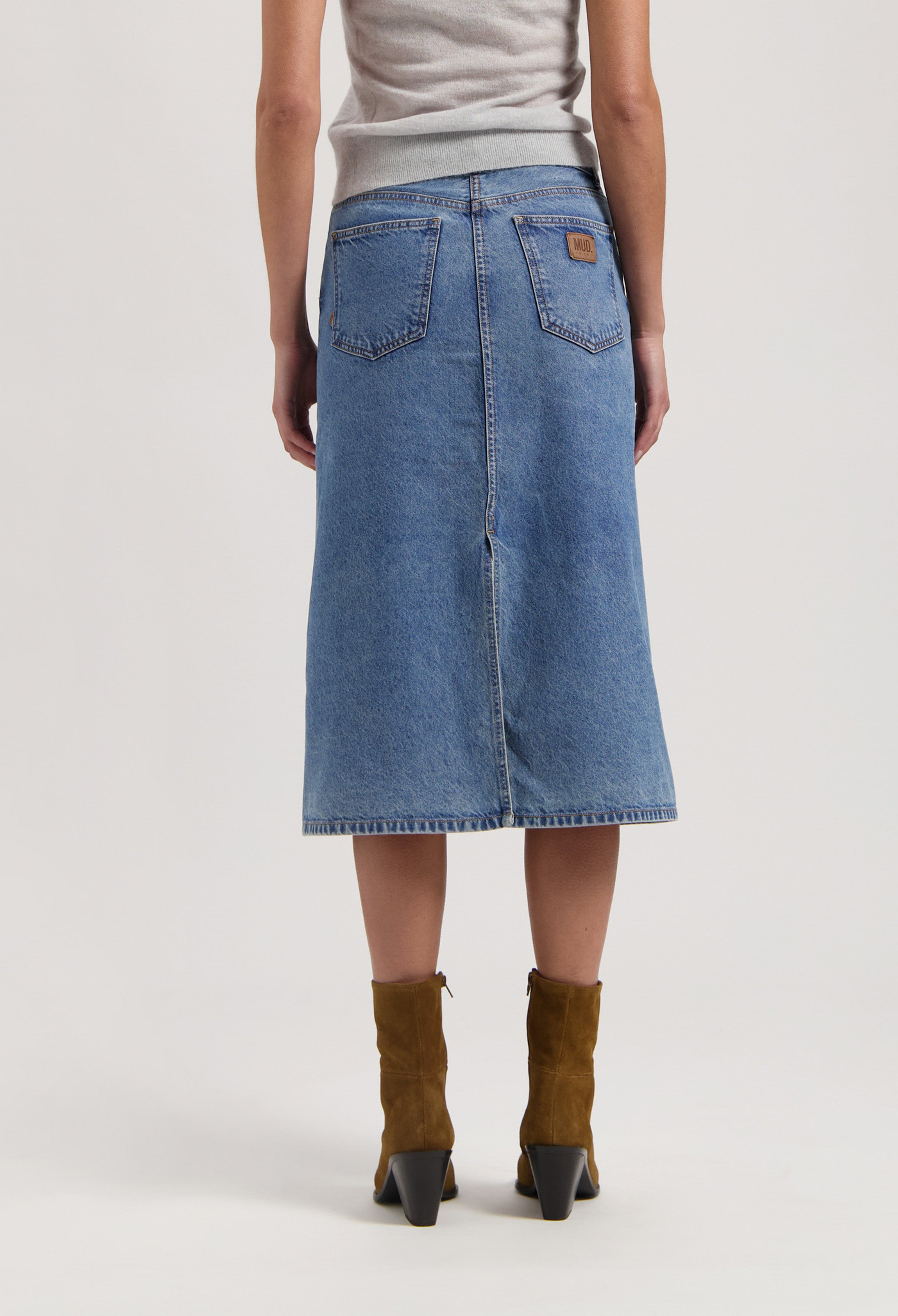 Mid-length blue denim skirt by MUD Jeans, featuring a classic straight cut, paired with brown suede ankle boots.