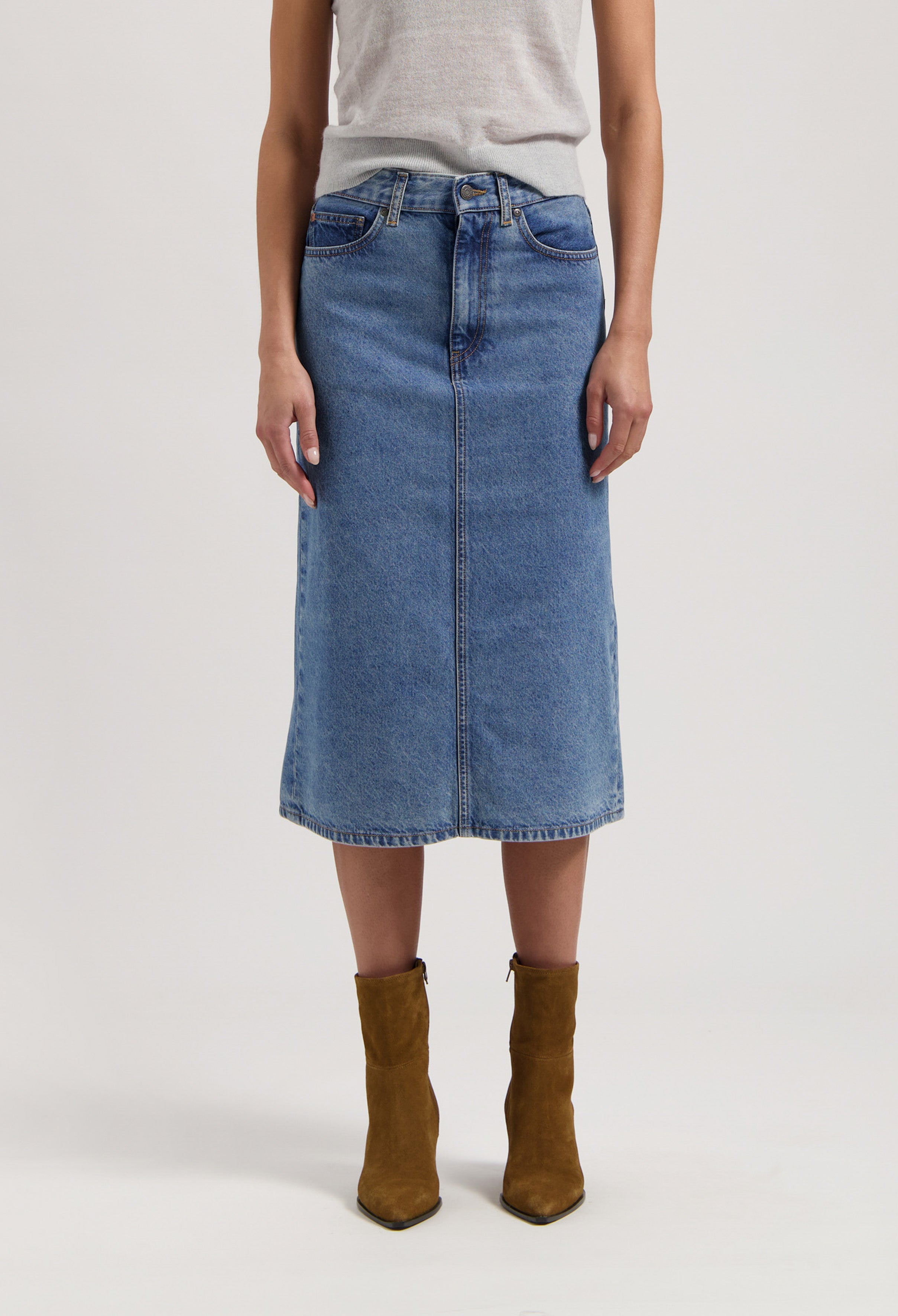 Denim midi skirt made from organic cotton in light blue, paired with gray sleeveless top and brown suede ankle boots.