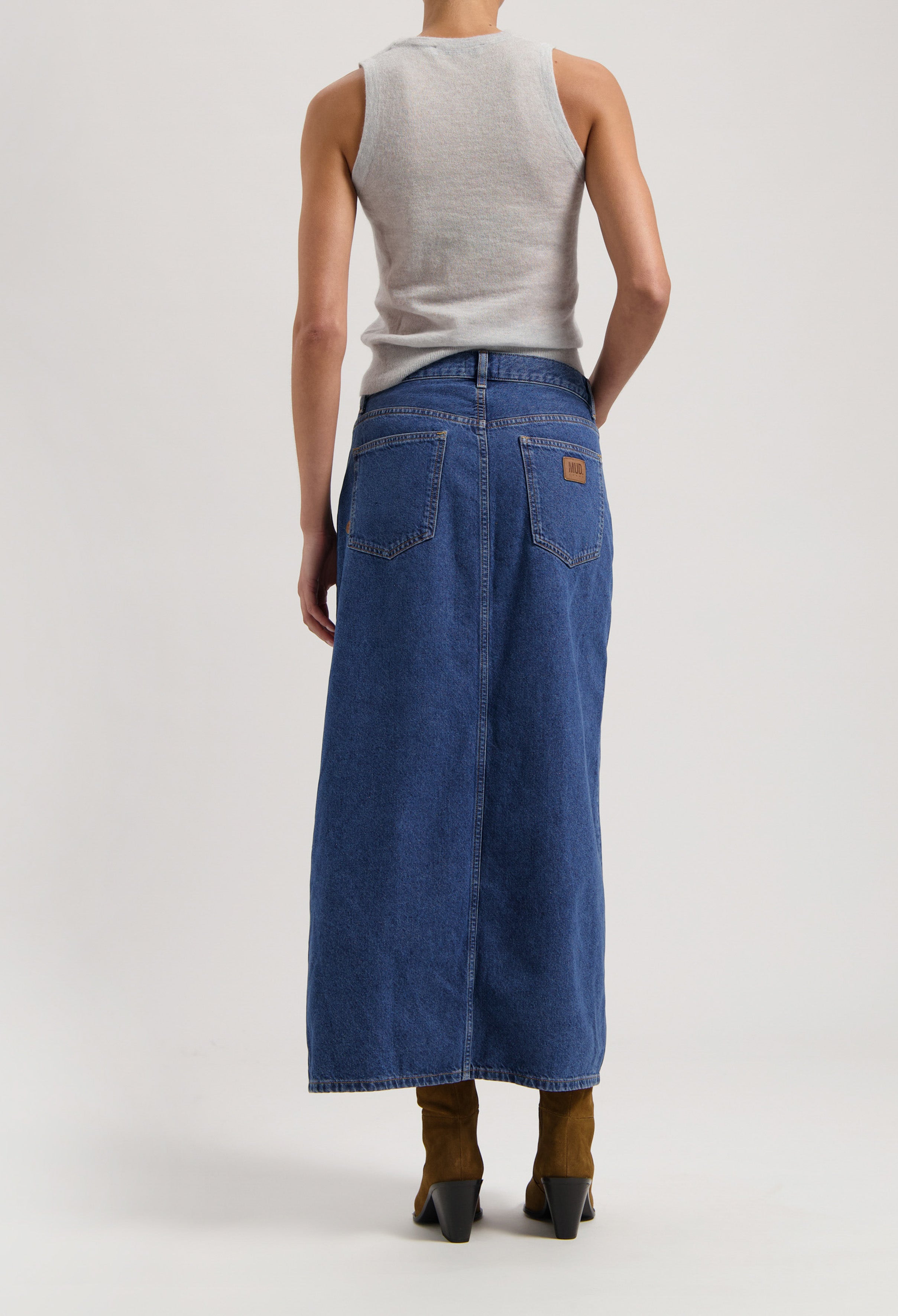 Sleeveless gray top with a blue denim maxi skirt featuring back pockets, styled with brown ankle boots.