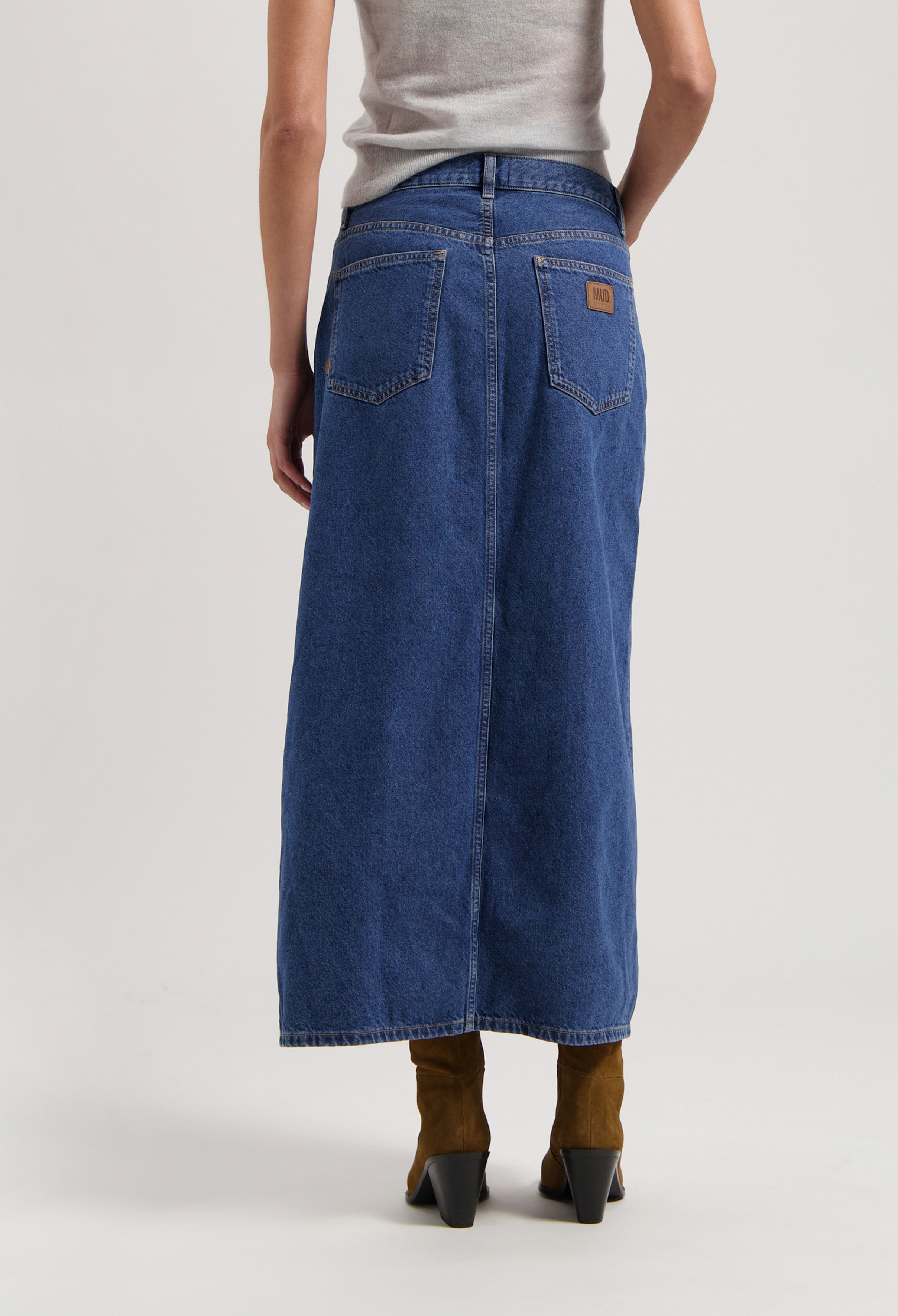 Mid-length blue denim skirt made from organic cotton, styled with a gray top and brown suede ankle boots.
