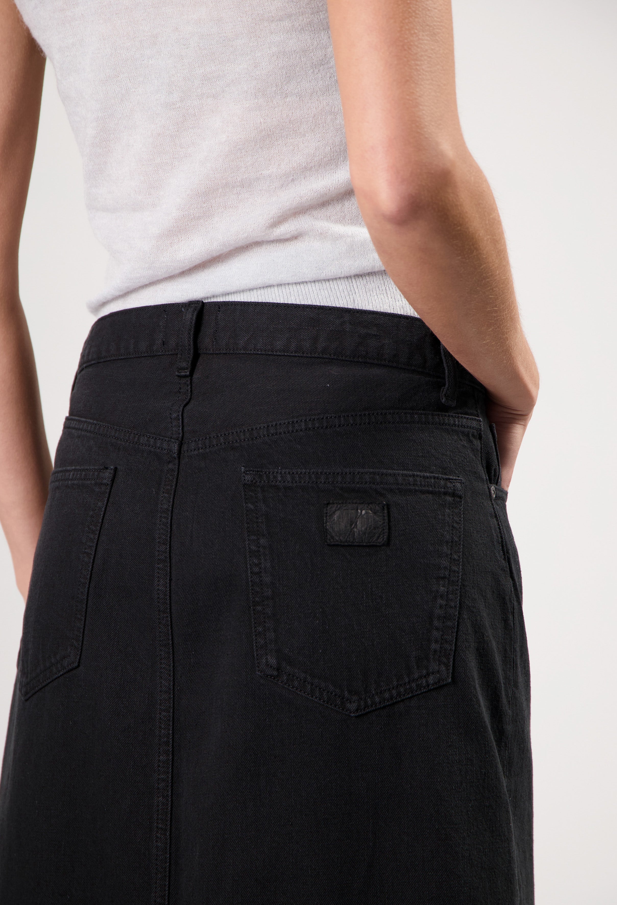 A close-up of a person wearing a fitted black denim skirt paired with a light gray sleeveless top, showcasing minimalist style.