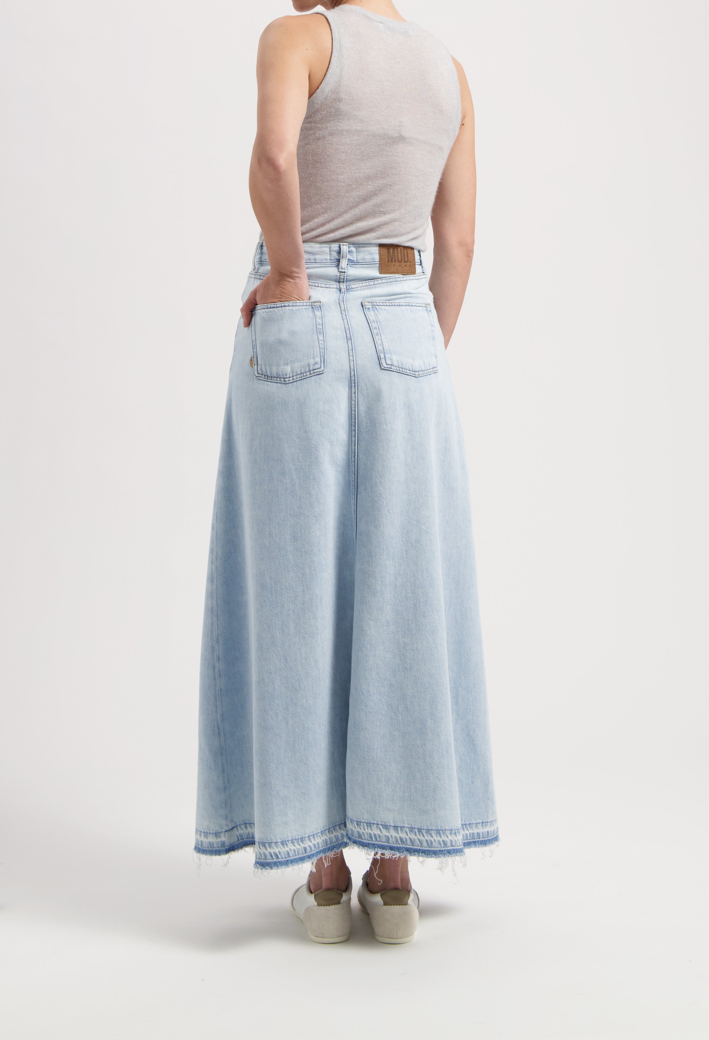 Light blue, high-waisted denim maxi skirt with raw hem, worn with a sleeveless gray top, showcasing sustainable MUD Jeans.