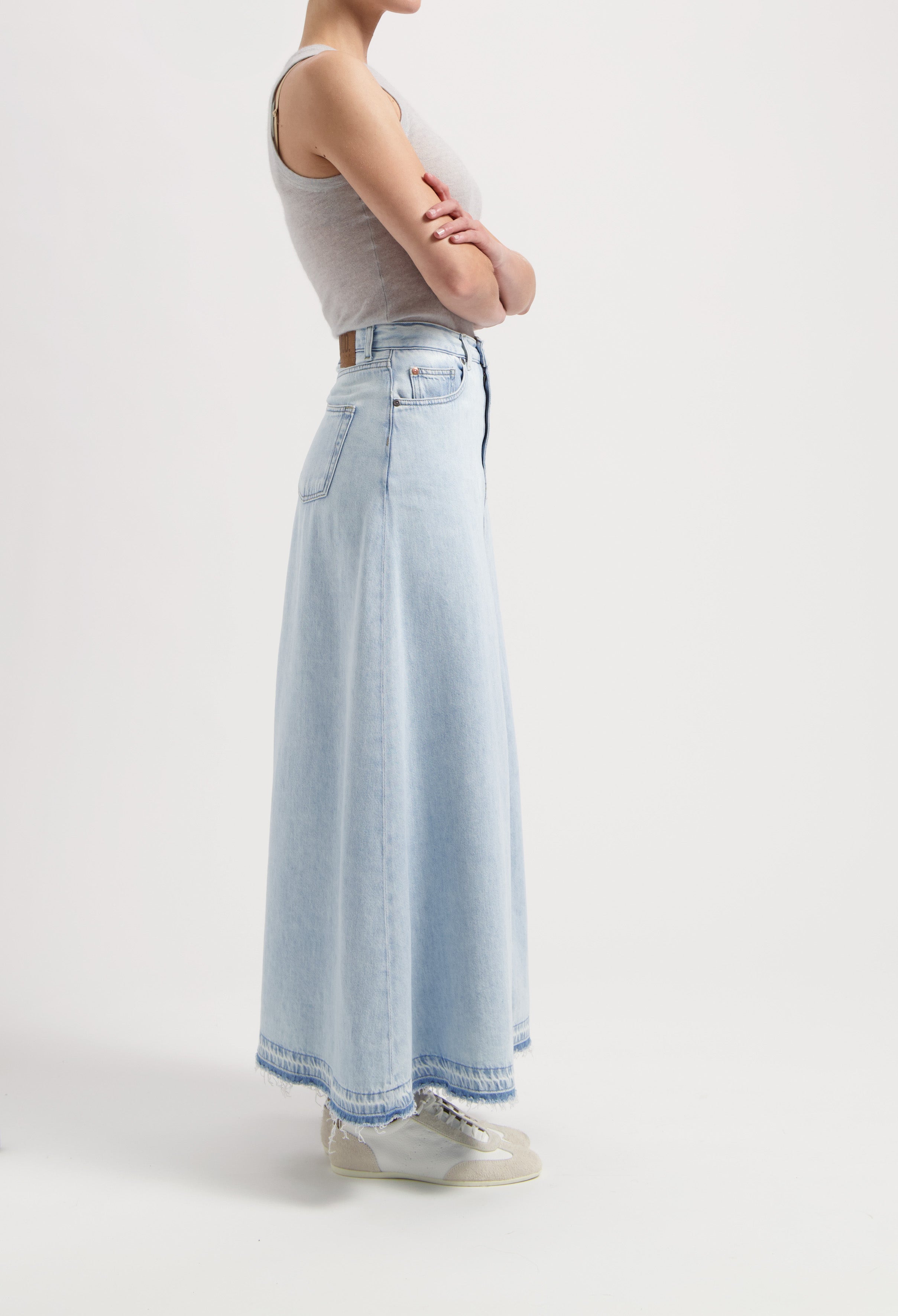 A-line maxi denim skirt in light blue with frayed hem, paired with a fitted sleeveless gray top and white sneakers.