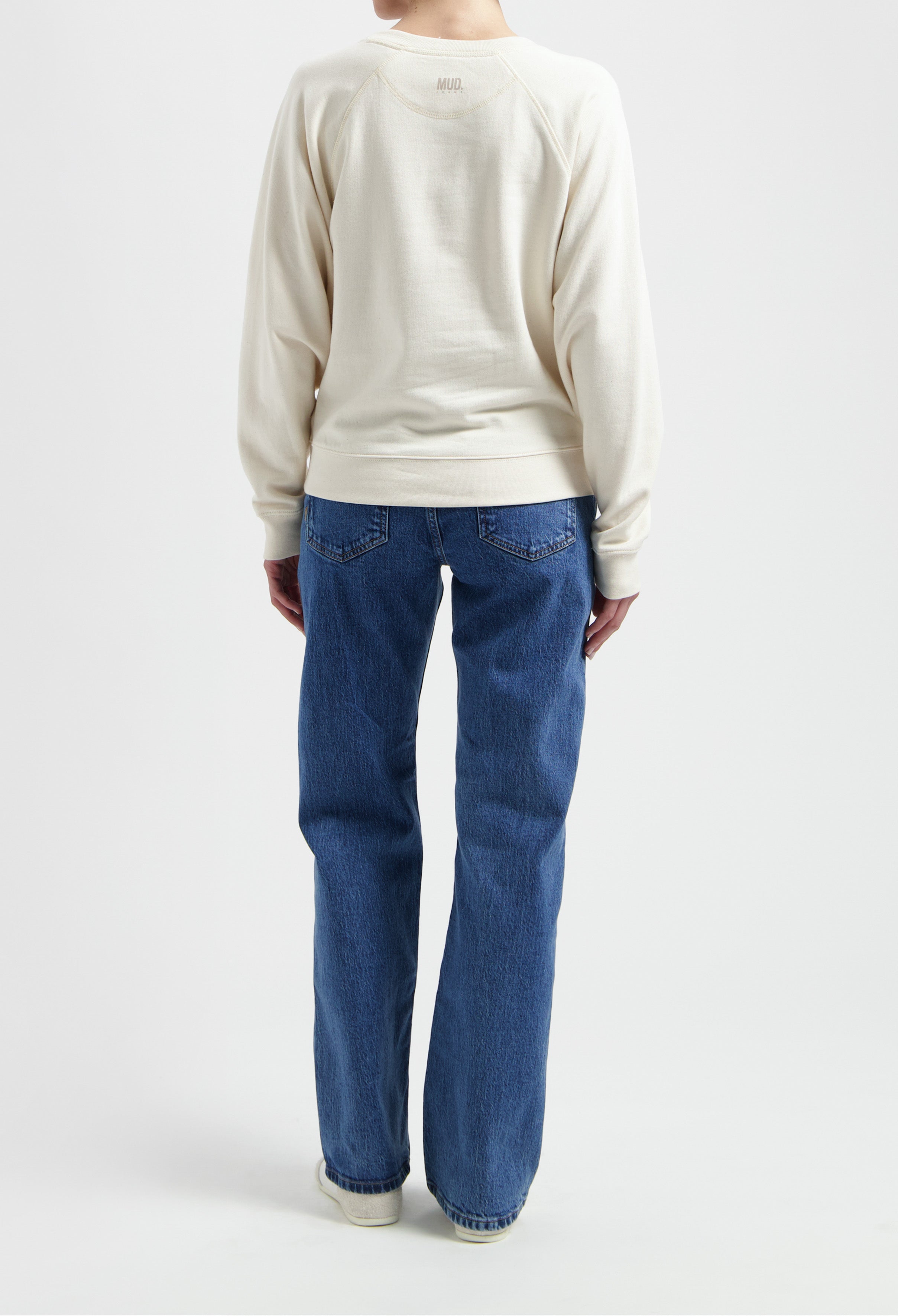 Back view of person wearing MUD Jeans, vintage blue denim, paired with cream organic cotton sweatshirt, showcasing relaxed fit style.