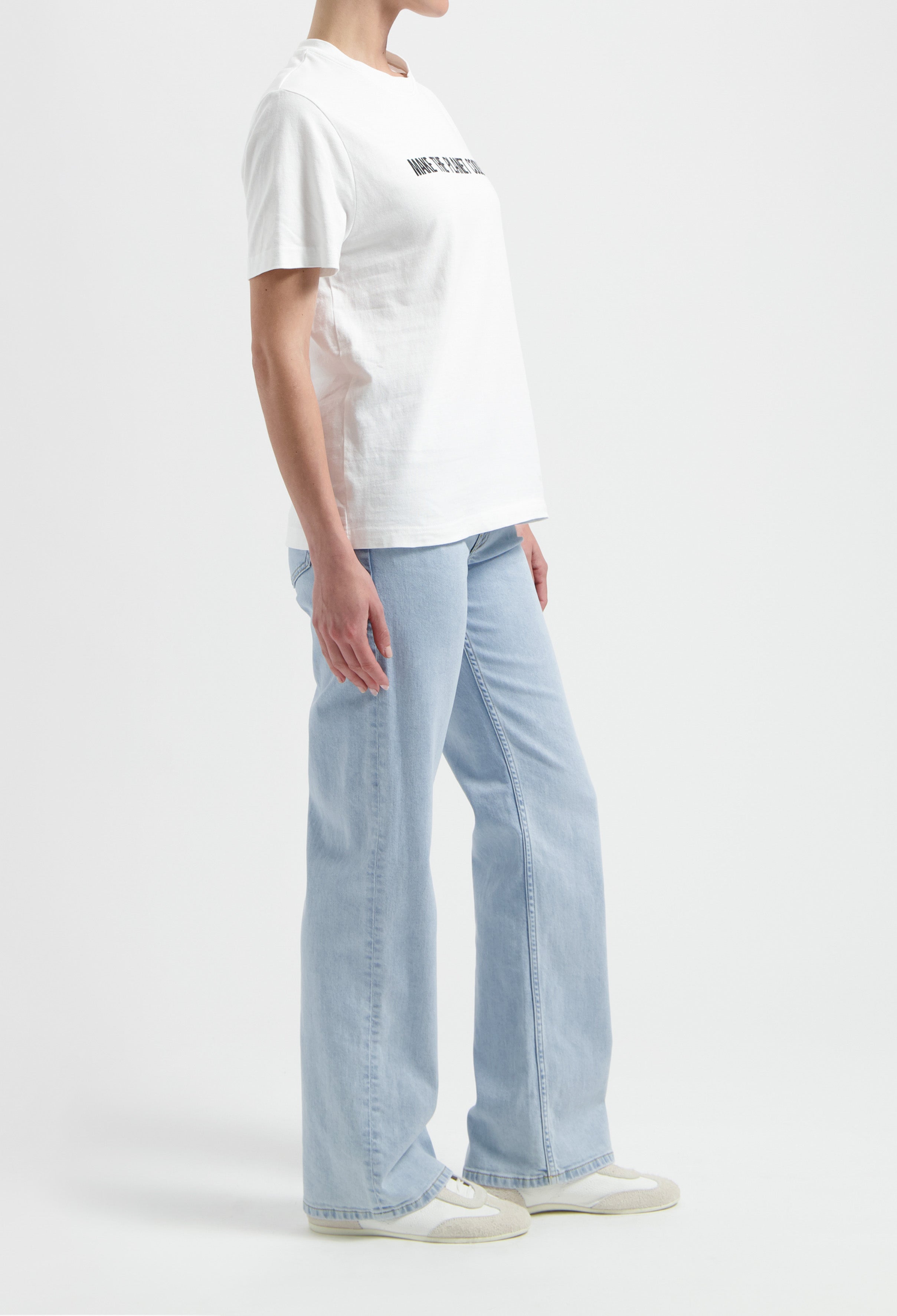 A casual outfit featuring a white cotton t-shirt with text, paired with light blue wide-leg jeans and white sneakers.