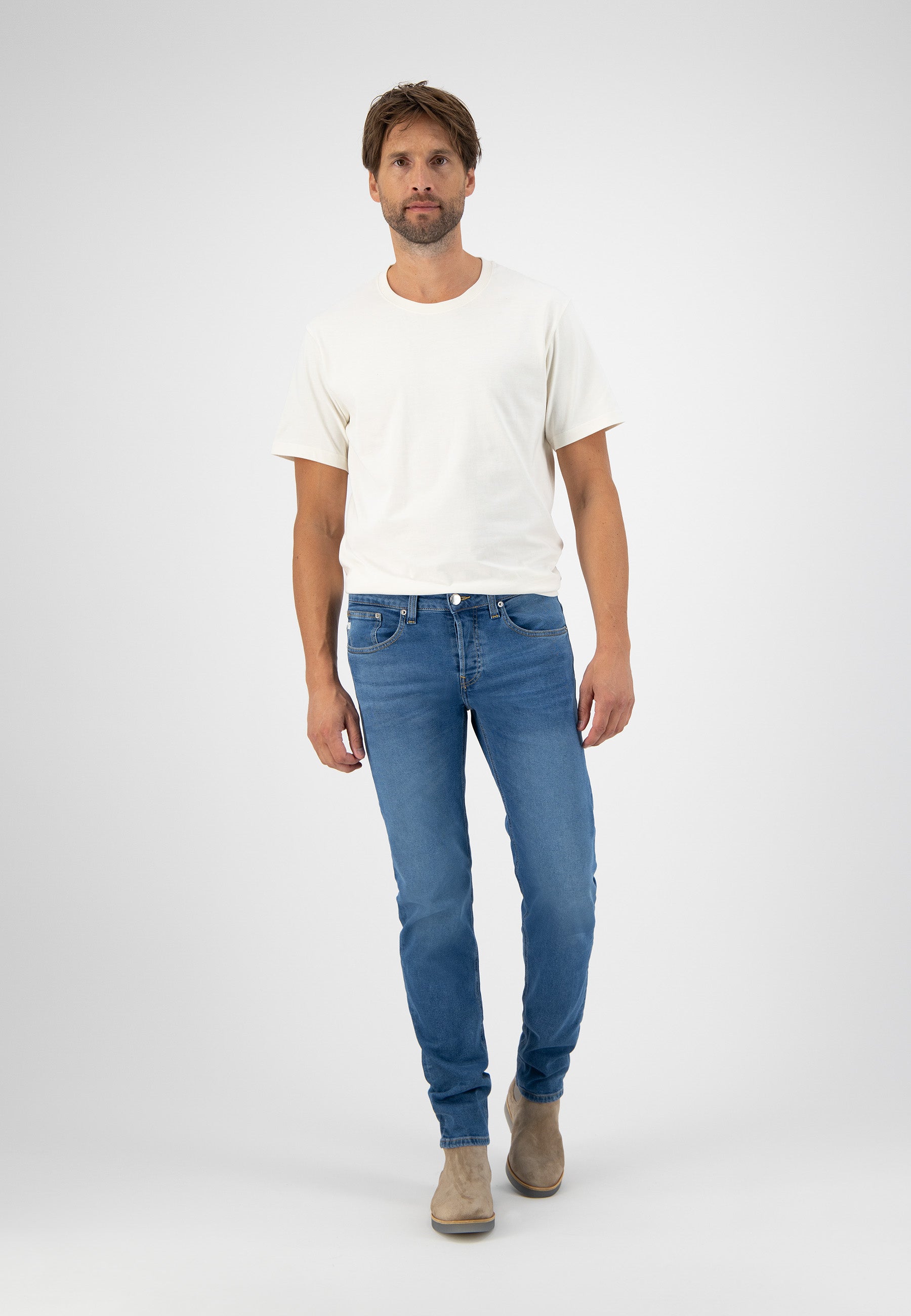 Sustainable MUD Jeans dark blue dungarees in eco-friendly denim, paired with a white long-sleeve shirt.