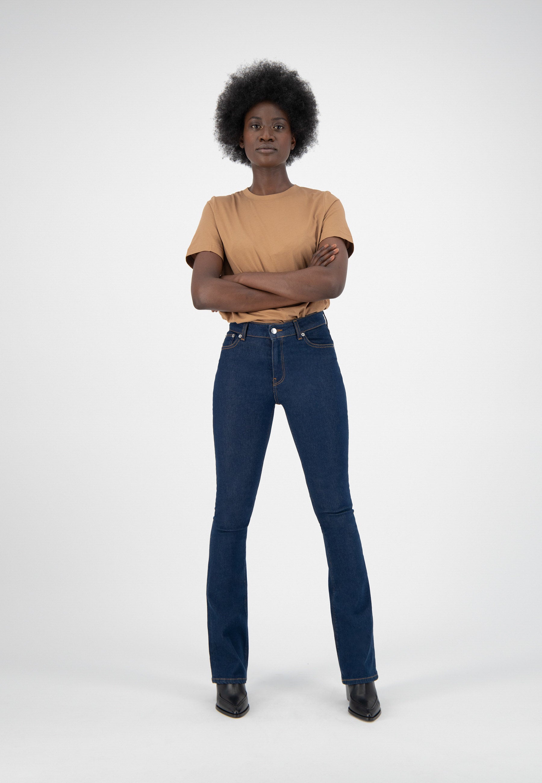 Model wearing a brown short-sleeve shirt with fitted dark blue jeans and black ankle boots against a white background.