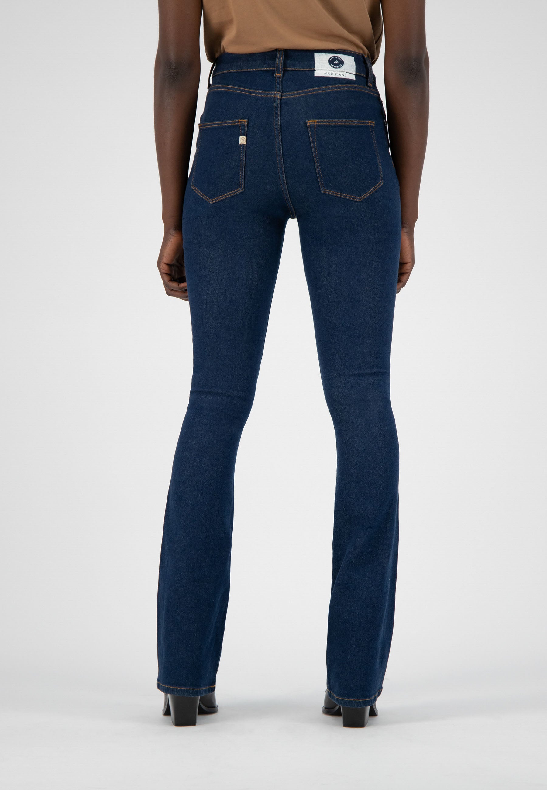 Back view of dark blue, eco-friendly denim jeans with bootcut fit, showcasing classic stitching and white brand label.