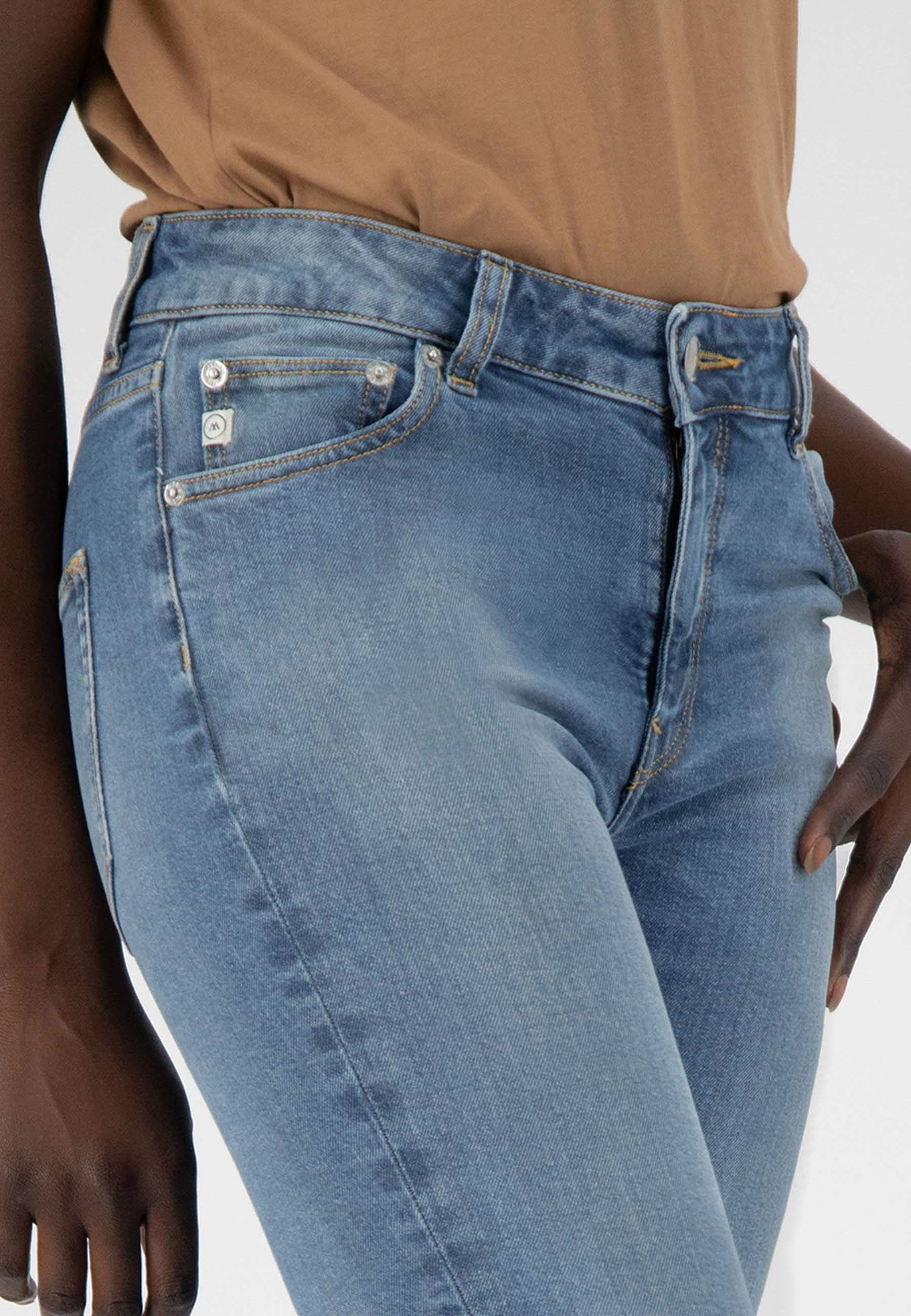 Close-up of light blue denim jeans with a high-rise waist and slim fit, paired with a tan top showing casual style.