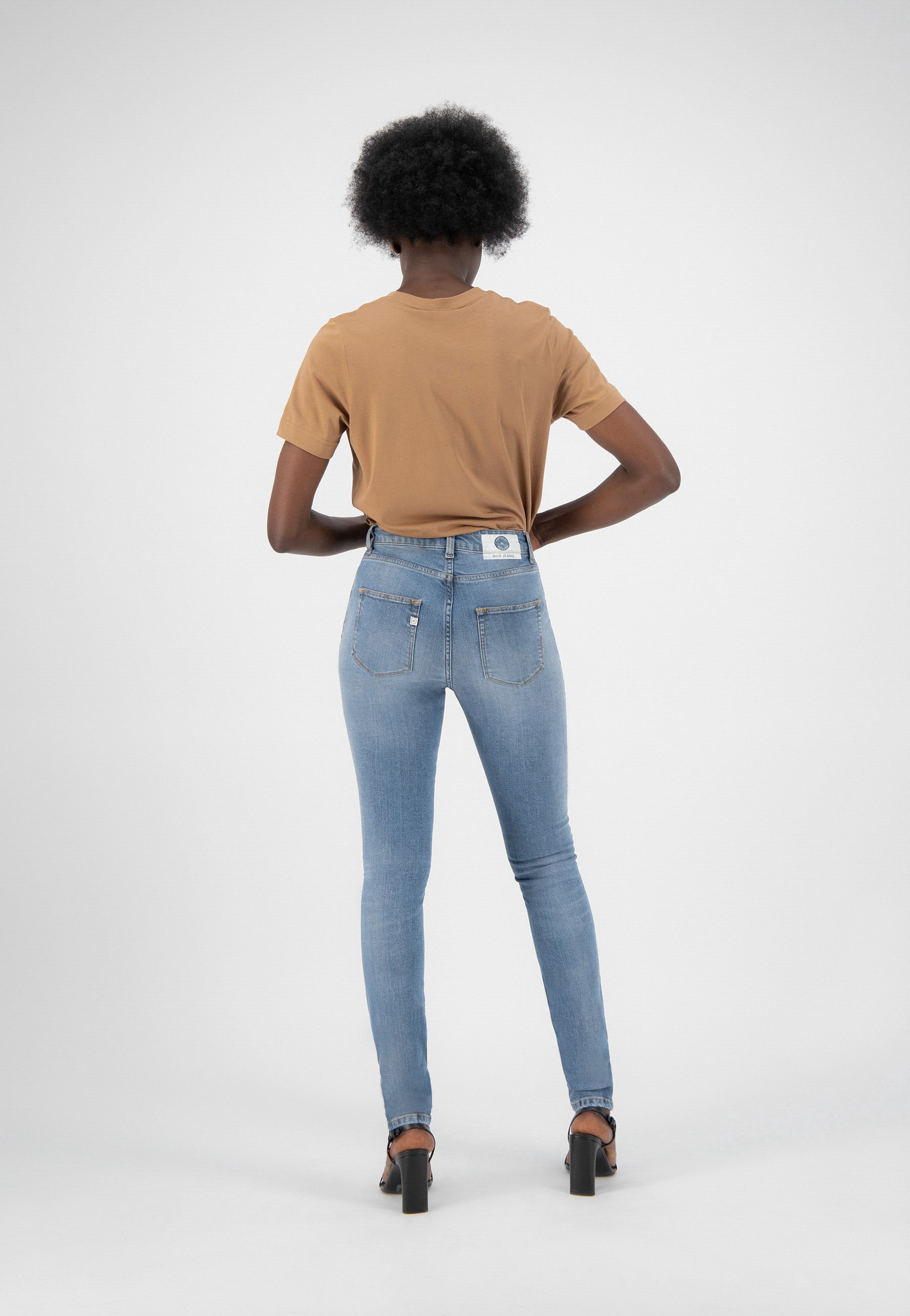 Model wearing light blue, high-waisted skinny jeans with a tan short-sleeve top, showcasing denim's back pocket details.