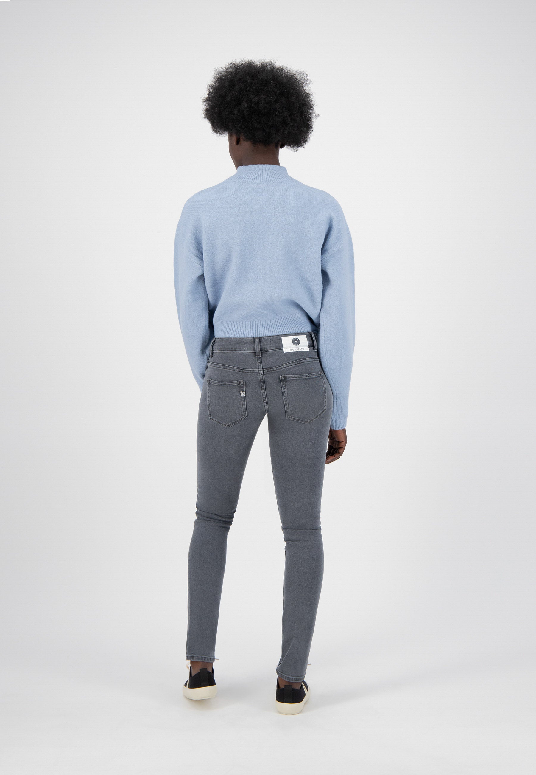Model wearing light blue sweater and gray slim-fit jeans, showcasing casual style with comfortable, modern clothing.