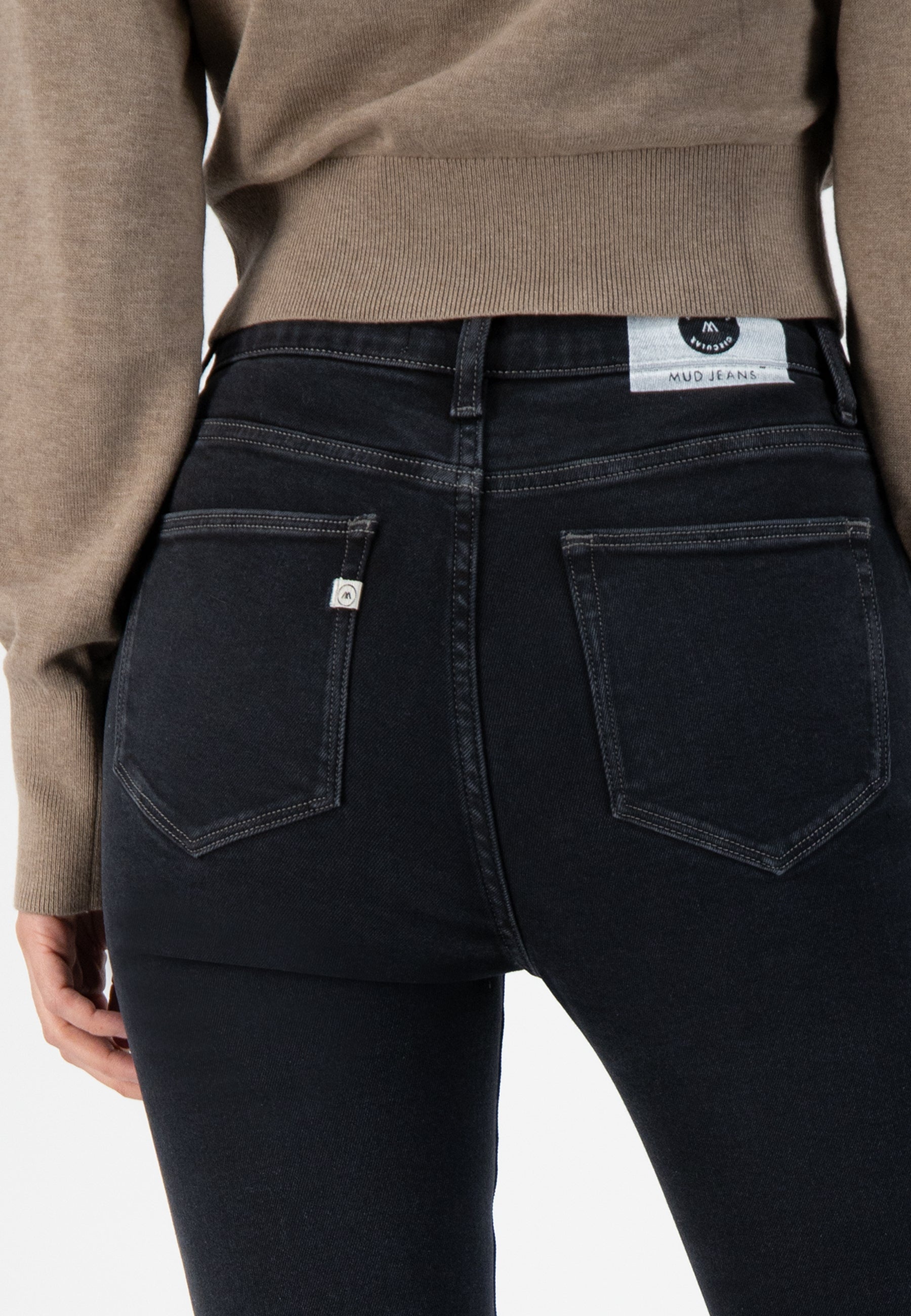 Stylish dark blue MUD Jeans crafted from organic cotton, featuring a slim-fit design worn with a cozy beige sweater.