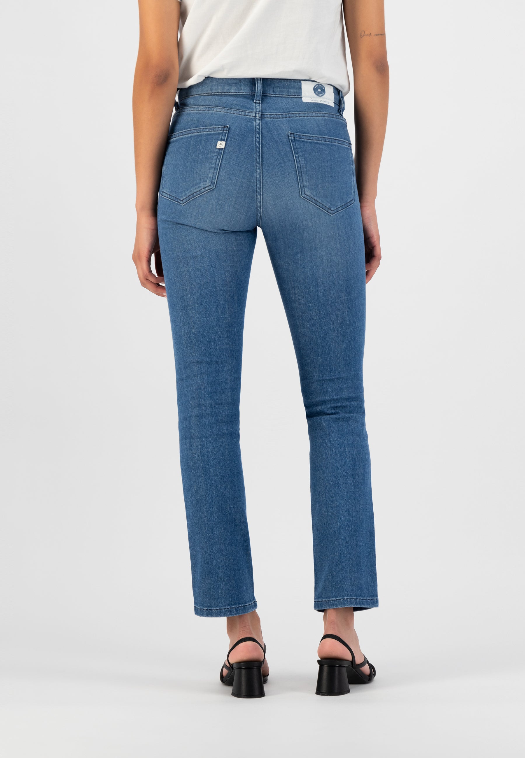 Mid-rise blue denim jeans with a straight leg fit, featuring back pockets and belt loops, worn with a white top and black sandals.