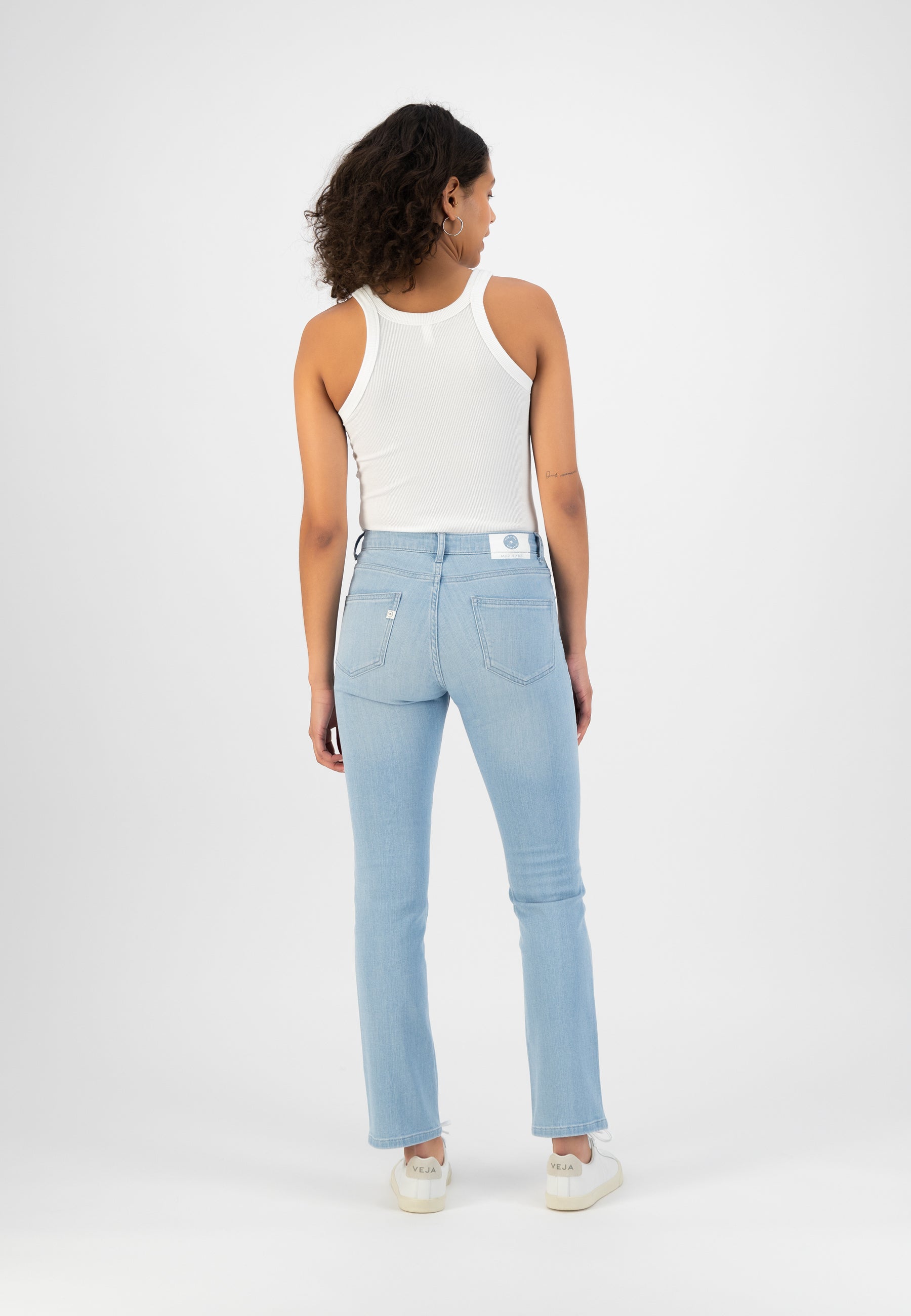 Light blue denim jeans with a straight fit, worn by a model in a white tank top and off-white sneakers, viewed from the back.