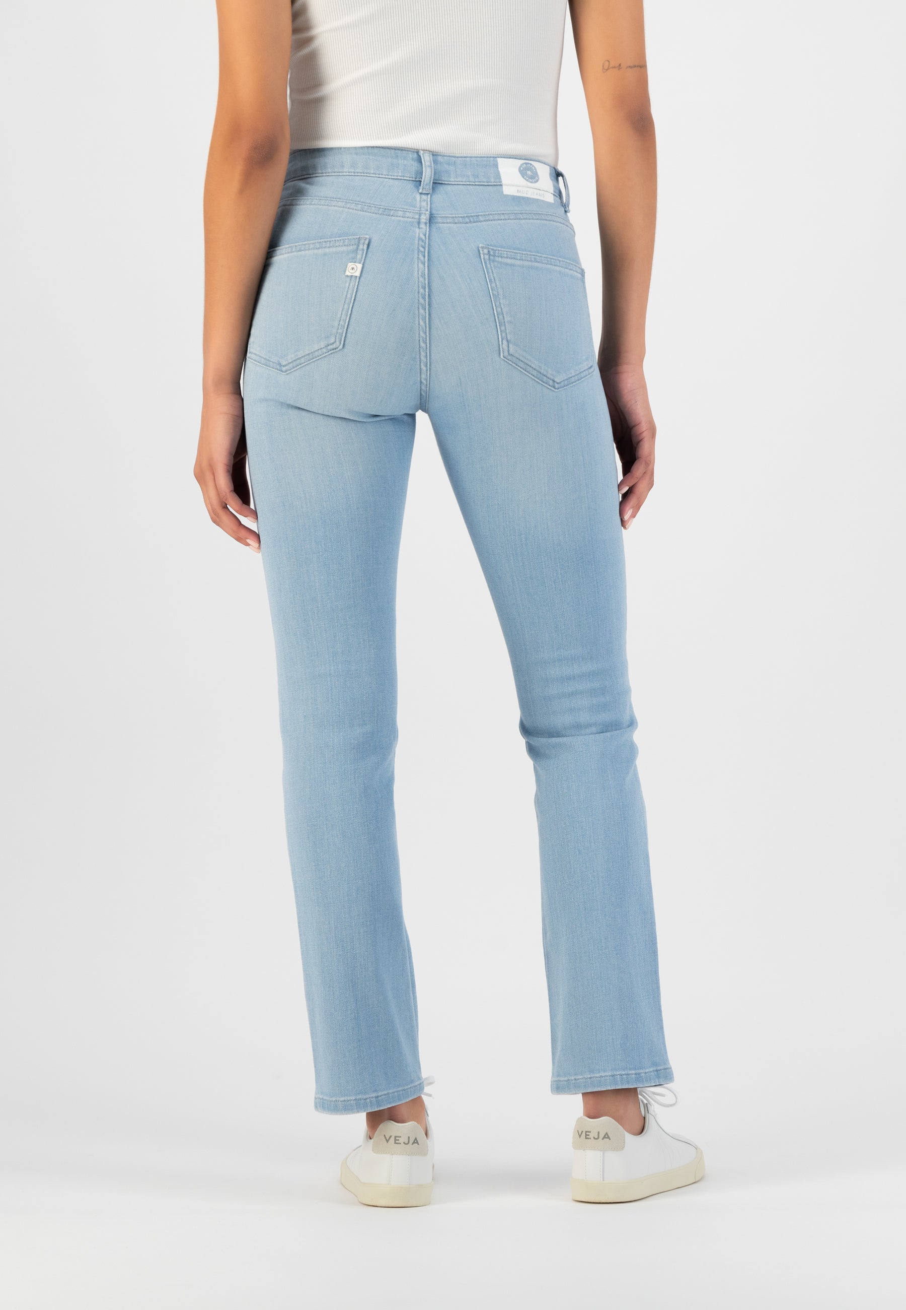 Light blue, high-waisted denim jeans with classic stitching, worn by a person in a white ribbed tank top and white sneakers.