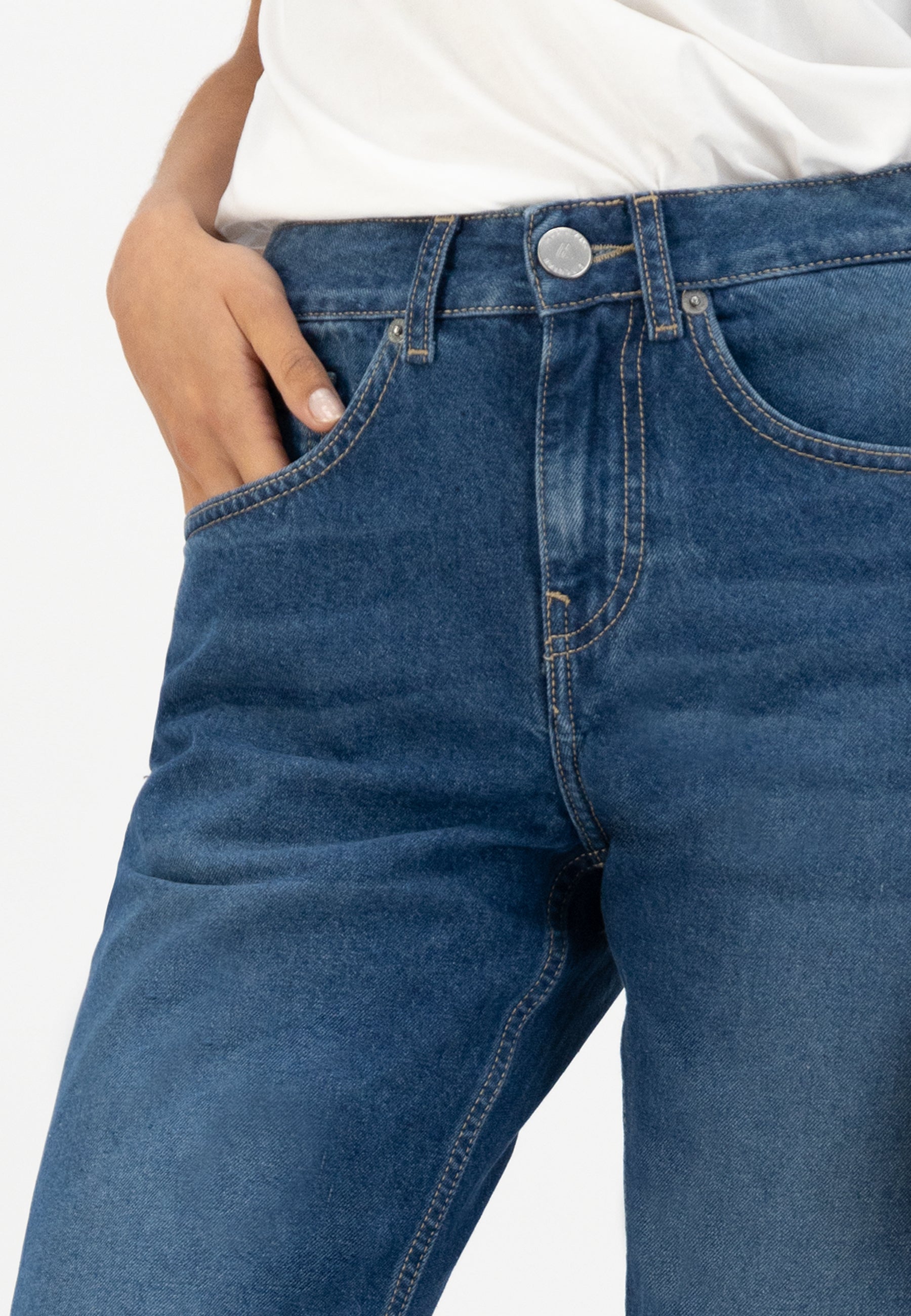 Close-up of blue denim jeans from eco-friendly fabric, showcasing classic five-pocket design paired with a white cotton shirt.